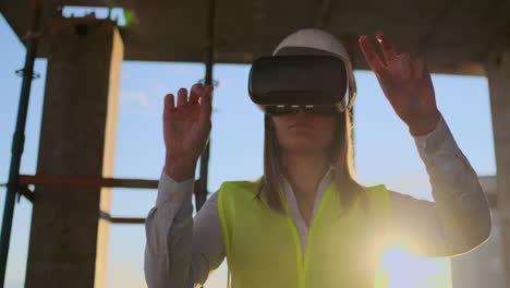 A-woman-engineer-at-a-construction-site-in-virtual-reality-glasses-moves-her-hands-simulating-the-work-of-the-interface-of-the-future-at-sunset
